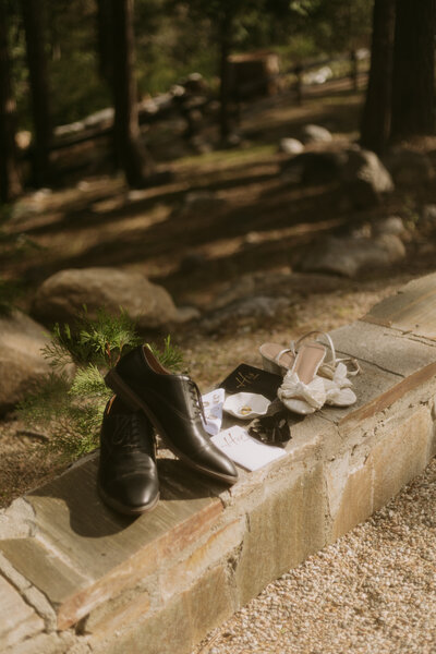 Details of the bride and grooms shoes resting on a ledge  with their vow books, rings, and bow tie.