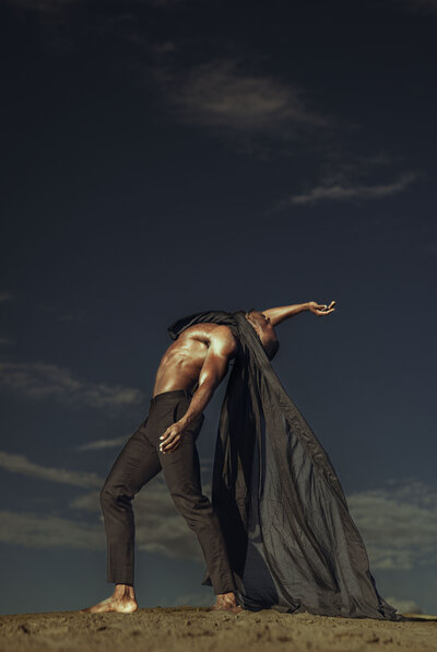 Man posing, bending back, black pants, black cape, blowing in the wind