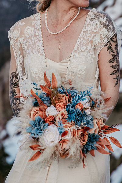 Close-up of a custom dried floral elopement bouquet in warm tones, held by the bride, captured by San Francisco elopement photographer Kristin Smith.