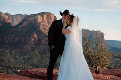 Bride kissing the cheek of her groom while he looks at the camera  with the sedona red rock in the background