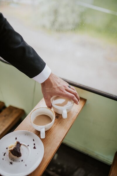 a groom reaching for a cup of coffee during bride and groom portraits. coffee shop stop on a wedding day