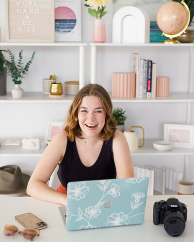 woman smiling while sitting at a desk in front of a laptop