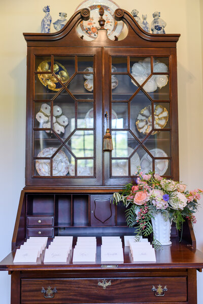 Antique wooden cabinet displaying a collection of decorative plates and shells behind glass doors.