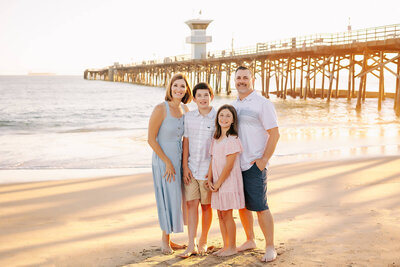 Family smiling posed next to Seal Beach Pier by Ashley Nicole.