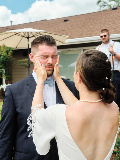 Bride rubs sunscreen onto the grooms face as a wedding toast occurs in the background