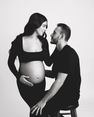 Couple embracing for their maternity session in black and white studio.