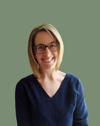 Portrait d’Aurélie Gignon, femme souriante aux lunettes et pull bleu marine, photographiée sur fond uni vert pour le blog de Lili Créa Design, consultante en branding et webdesign en Loire-Atlantique