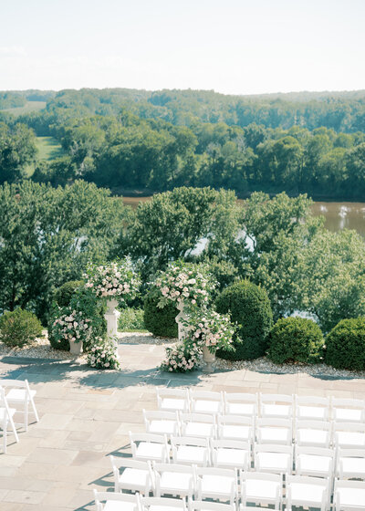 Bride and groom embrace under large green trees.