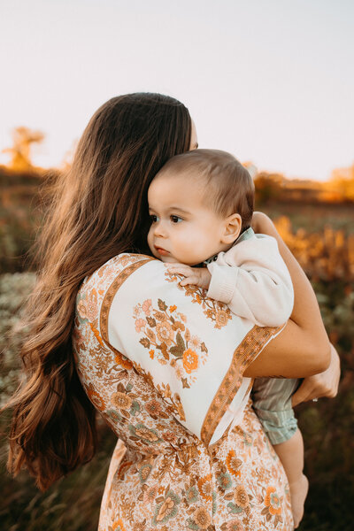 Mother holding her infant in a field at sunset.