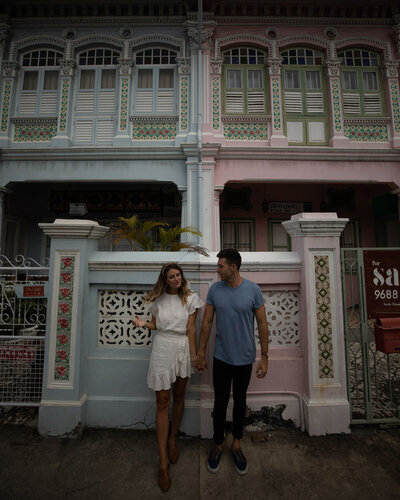 man and woman holdings hands in front of blue and pink building