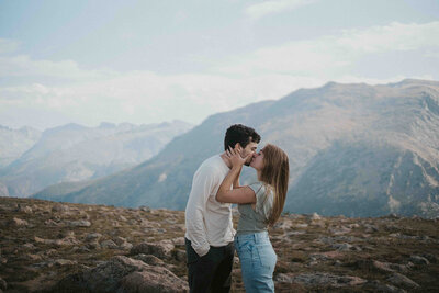 Couple faces each other and kisses in front of rocky mountain range