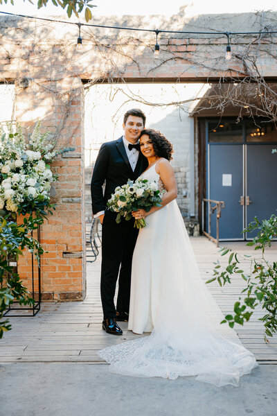 Bride with a light pink bouquet and groom in a navy suit smiling at each other