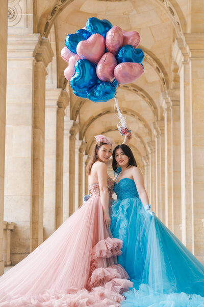Mother and daughter wearing matching pink and blue princess dresses with heart balloons in Louvre gallery Paris