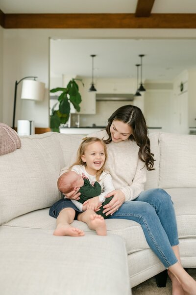 Mom snuggles on couch with two kids at milwaukee lifestyle newborn shoot