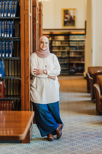 woman in hijab leans against stacks in library