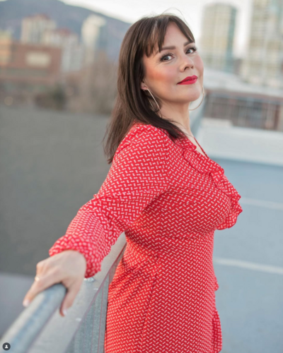 Modern portrait of makeup artist Jenny McKinney posing in red dress in an urban outdoor setting .