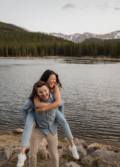 Couple laughing together in front of water and mountains during their engagement session at Echo Lake in Colorado