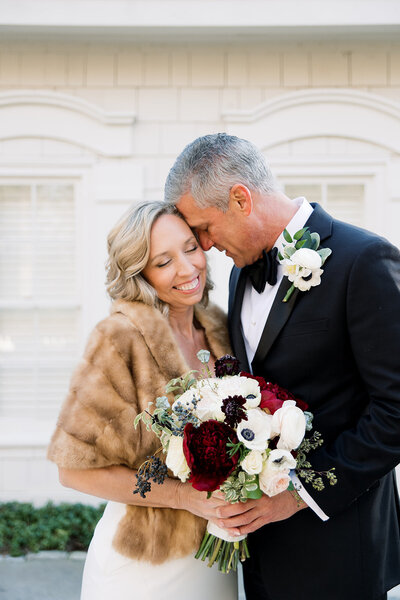 woman in fur coat smiling while man in black tux hugs her