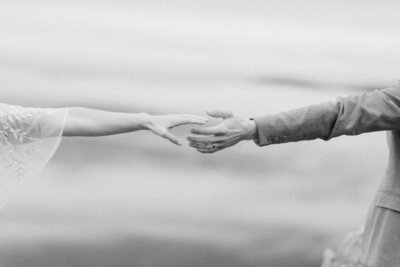 Bride and groom standing hand in hand with a mountain lake behind them during their intimate Virginia elopement, photographed in natural light and soft tones.

