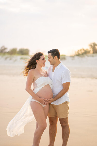 Couple having maternity photoshoot with family on the beach during sunset.