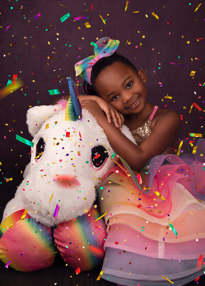 girl-hugging-unicorn-stuffed-animal-in-rainbown-dress-with-rainbow-confetti-in-arlington-tx-studio