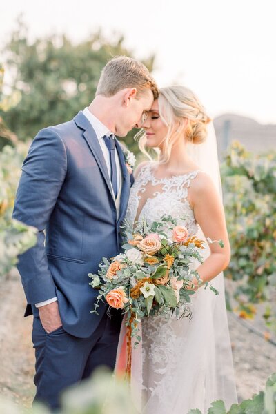 The bride holds a large fall color themed bouquet as she stands next to her groom.