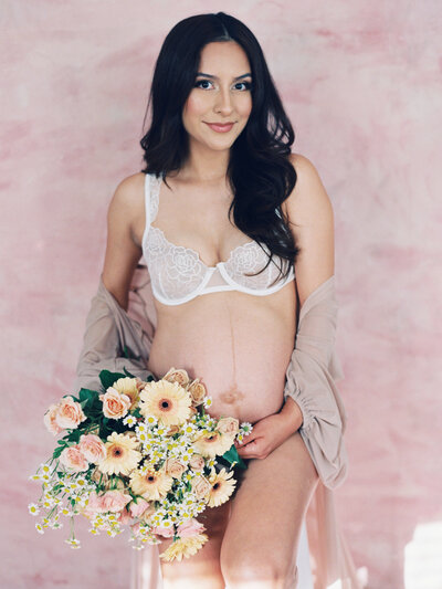 A maternity motherhood session with a hand painted pink backdrop and delicate bouquet in boudoir outfit