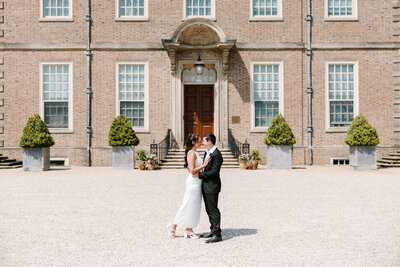 Photo of bride and groom standing in front of large mansion taken by Best wedding photographer in Portland Maine