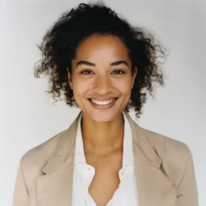 Professional headshot of woman with curly hair smiling brightly against plain gray studio background new jersey.