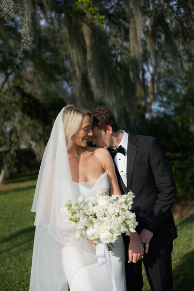 husband kissing his wife on the shoulder while she holds flowers