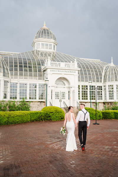 A bride and groom walk towards the Franklin Park Conservatory Palm House during golden hour