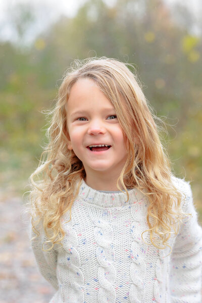 A dreamy portrait of a young girl with curly wavy hair smiling and laughing during a photo session with Shannon Cliffe Photography