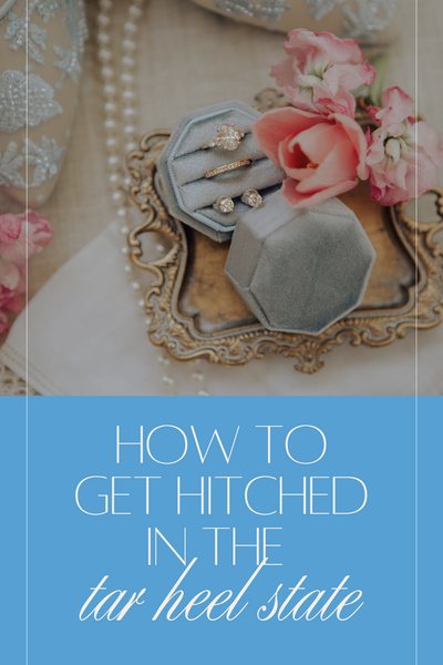 A set of wedding rings in a blue velvet ring box surrounded by pink flowers.