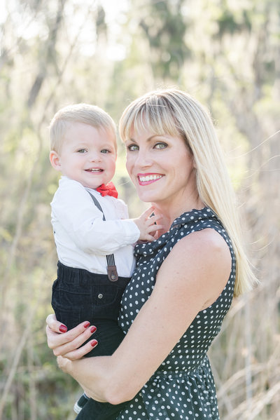 Mother in polka dot dress holds toddler son in white button down and red bow tie