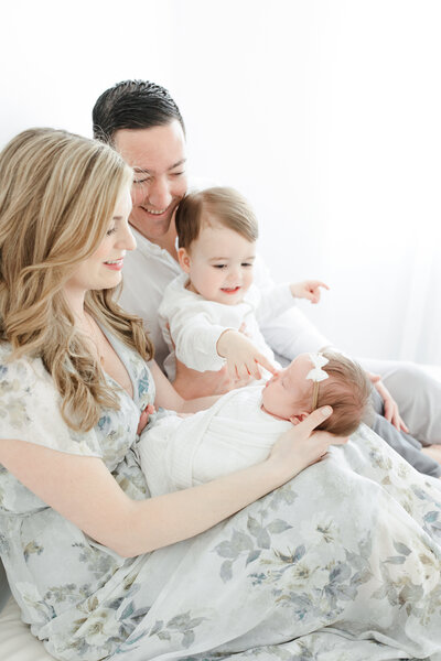Parents hold their toddler son and sleeping newborn daughter during newborn portrait session