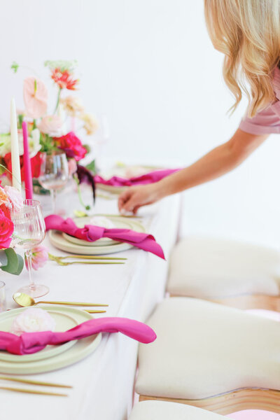 Woman setting a table with pink napkins, gold silverware, pink candles, and pink floral centerpieces