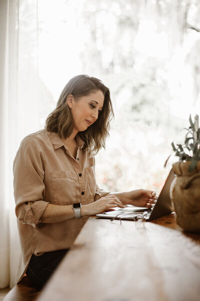 Woman sitting at a table slightly smiling and looking at a laptop