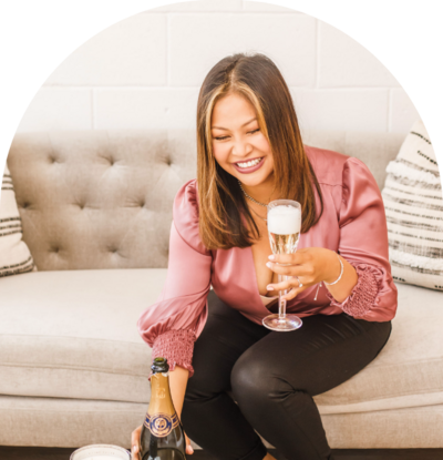 woman wearing a pink silk long sleeves top holding a glass of champagne while sitting on the couach