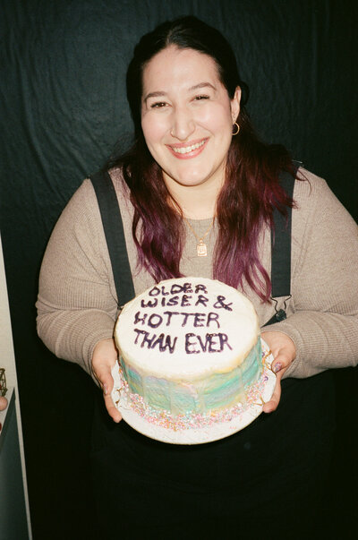 A person smiling and holding a small cake.