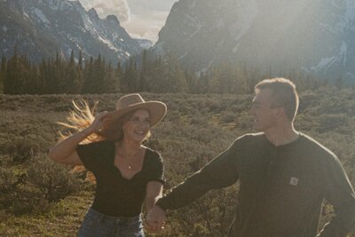 couple running in field with mountains in the background