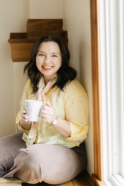 portrait of Aspen Colorado wedding photographer Mrs. Ferree Photography holding a coffee mug sitting in a window sill