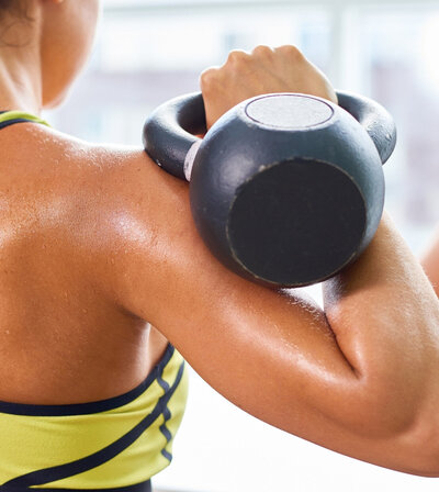Close-up of a woman holding a kettlebell in the rack position on her shoulder, ready to press, showcasing confident, strong movement for midlife fitness.