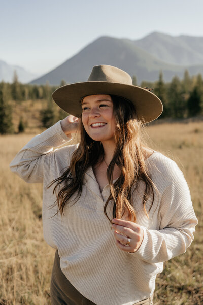Sydney Breann smiles with her hand on her hat. Montana Elopement Photographer.