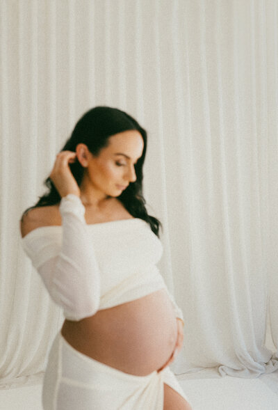 a film photograph of a pregnant mother wearing a white top and white skirt posing with her hand behind her ear during a studio maternity photoshoot in christchurch with lucy jane photography