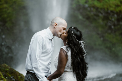 a bride and groom kiss at the base of a gushing waterfall