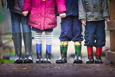 Children of different ages playing outside in rain boots during a rainy day at sliding scale childcare program in East Dallas, Dallas, TX, supporting early childhood education.