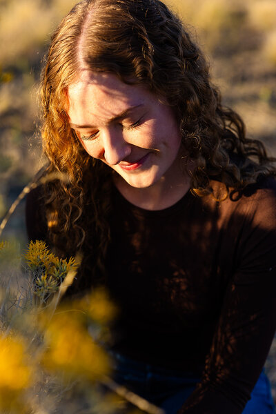 Haylee is looking down at some sagebrush in the Boise foothills. The sun is shining on her face.