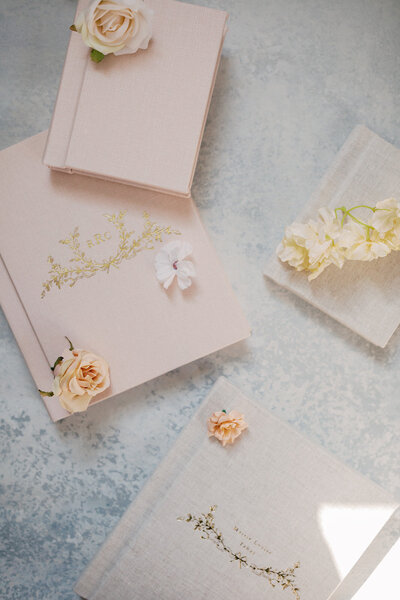 Light pink linen albums lay on a blue backdrop with florals.