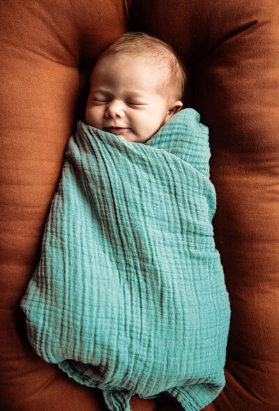 newborn swaddled in blue blanket on orange pillow