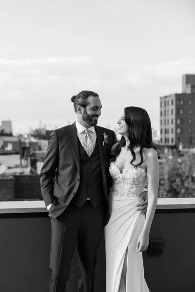 Black and white image of bride and groom looking at each other with a city backdrop